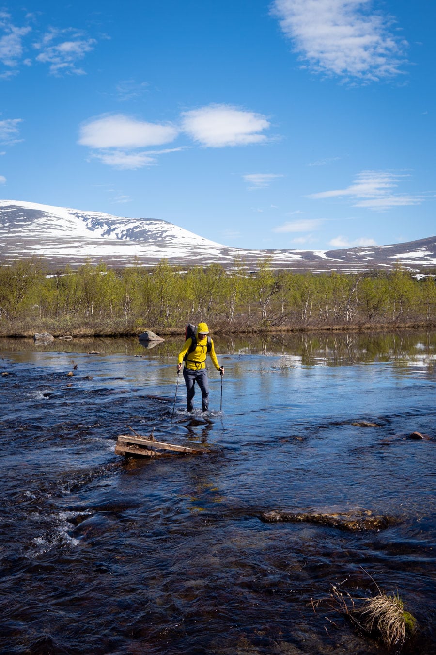 Hiker in lapland crossing a stream